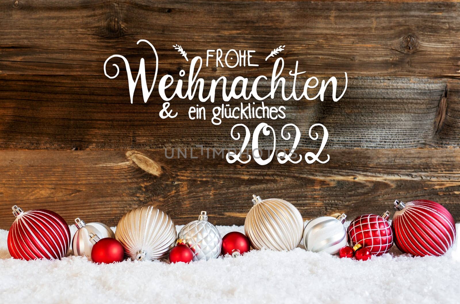 German Calligraphy Frohe Weihnachten Und Ein Glueckliches 2022 Means Merry Christmas And A Happy 2022. Rustic Brown Wooden Backgroud. Red And White Festive Christmas Ball Ornament On Snow.