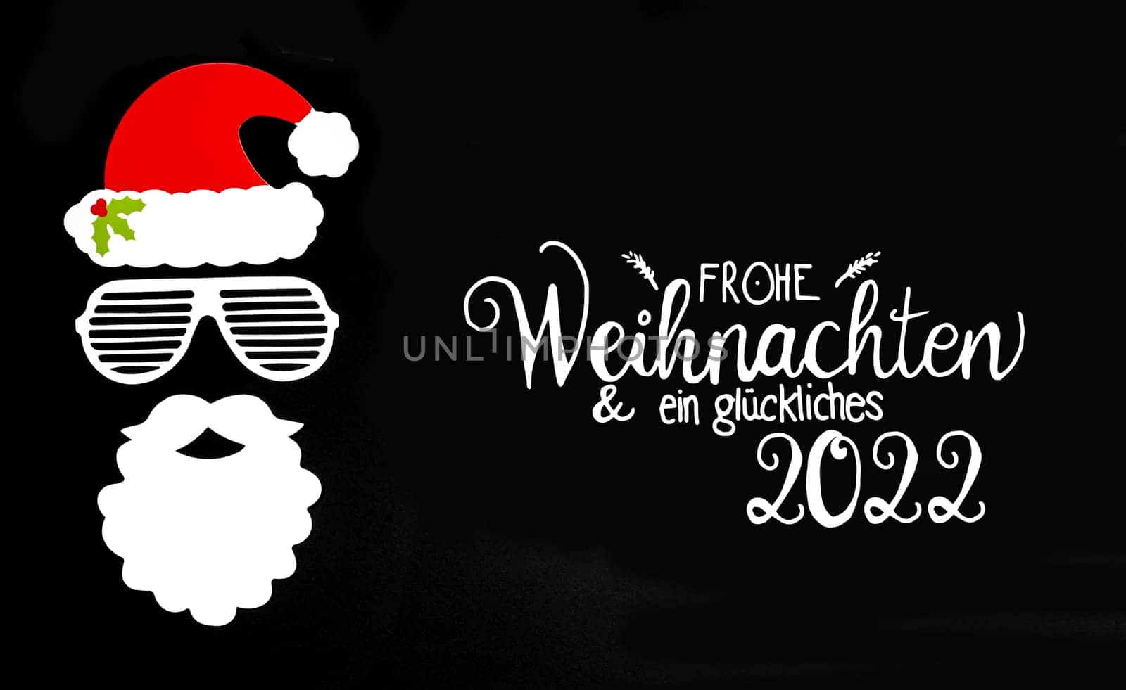 German Und Ein Glueckliches 2022 Means Merry Christmas And A Happy 2022. Santa Claus Paper Mask With Christmas Decoration And Accessories. Black Paper Background