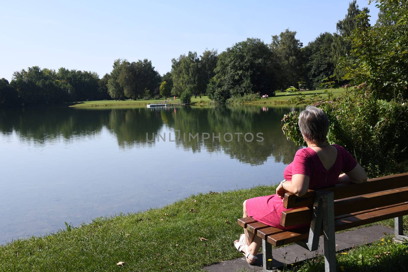 Natural springs feed the Germeringer See with water. The local recreation area near the city of Germering is in the Fürstenfeldbruck district in Bavaria. A woman looks out over the water.
