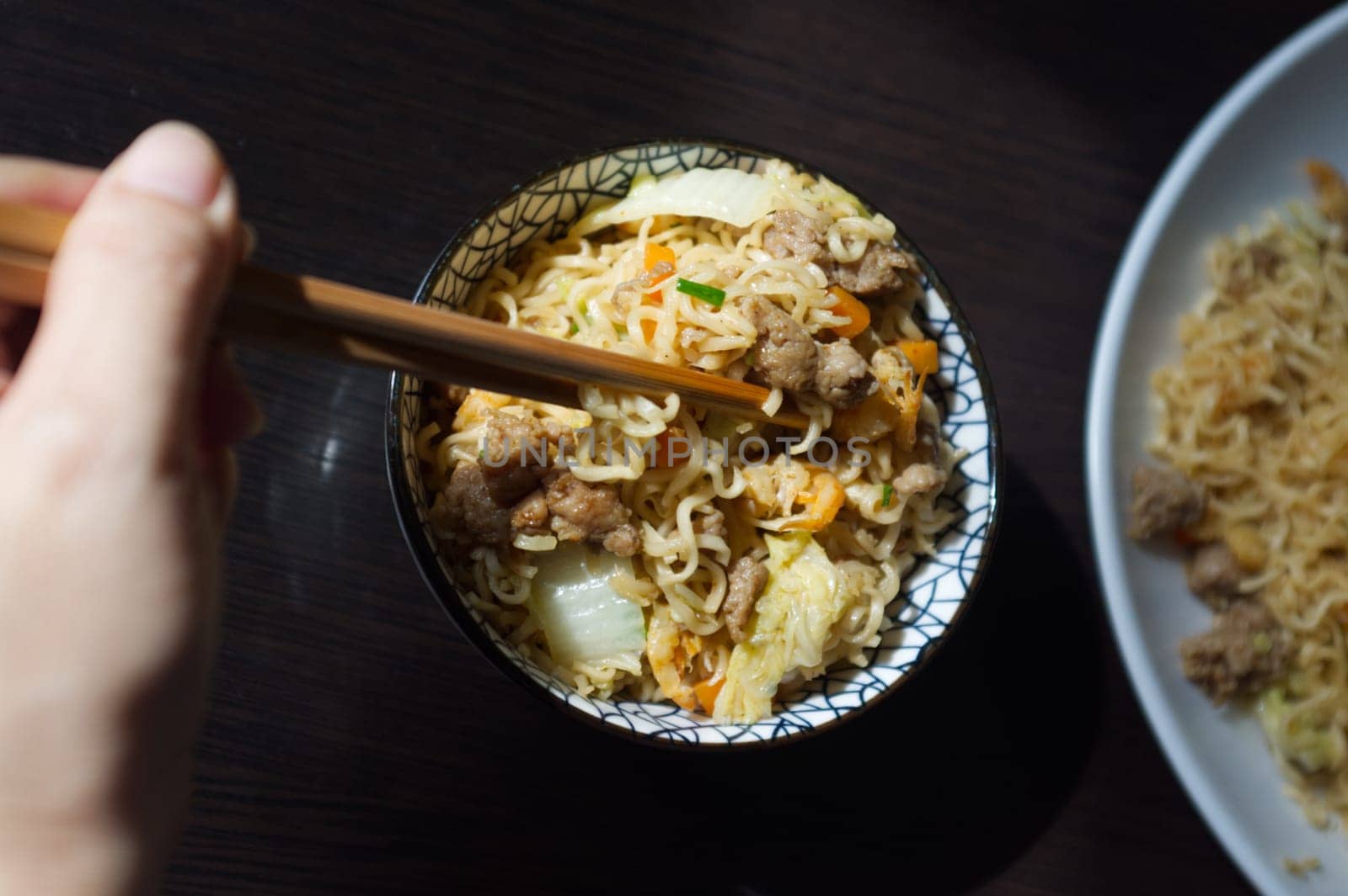 Woman's hand holding chopsticks of instant noodles.