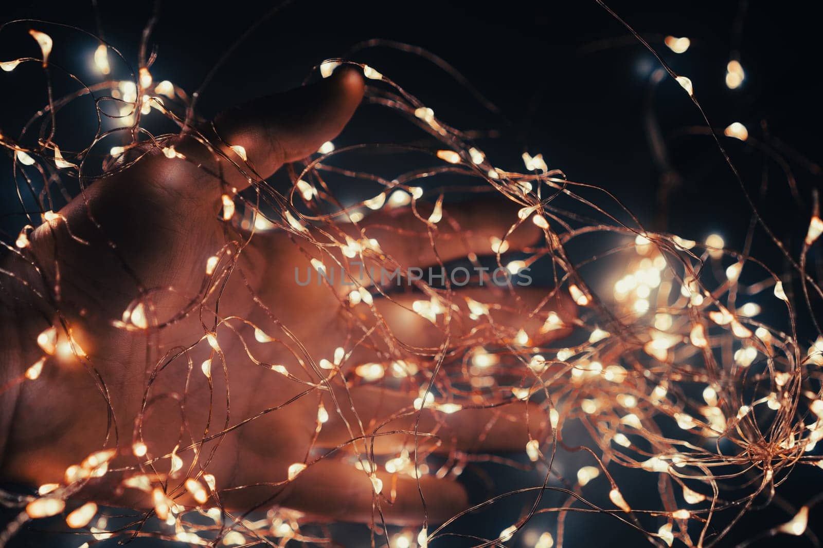closeup of Caucasian male hand covered in small garland of Christmas lights in the dark