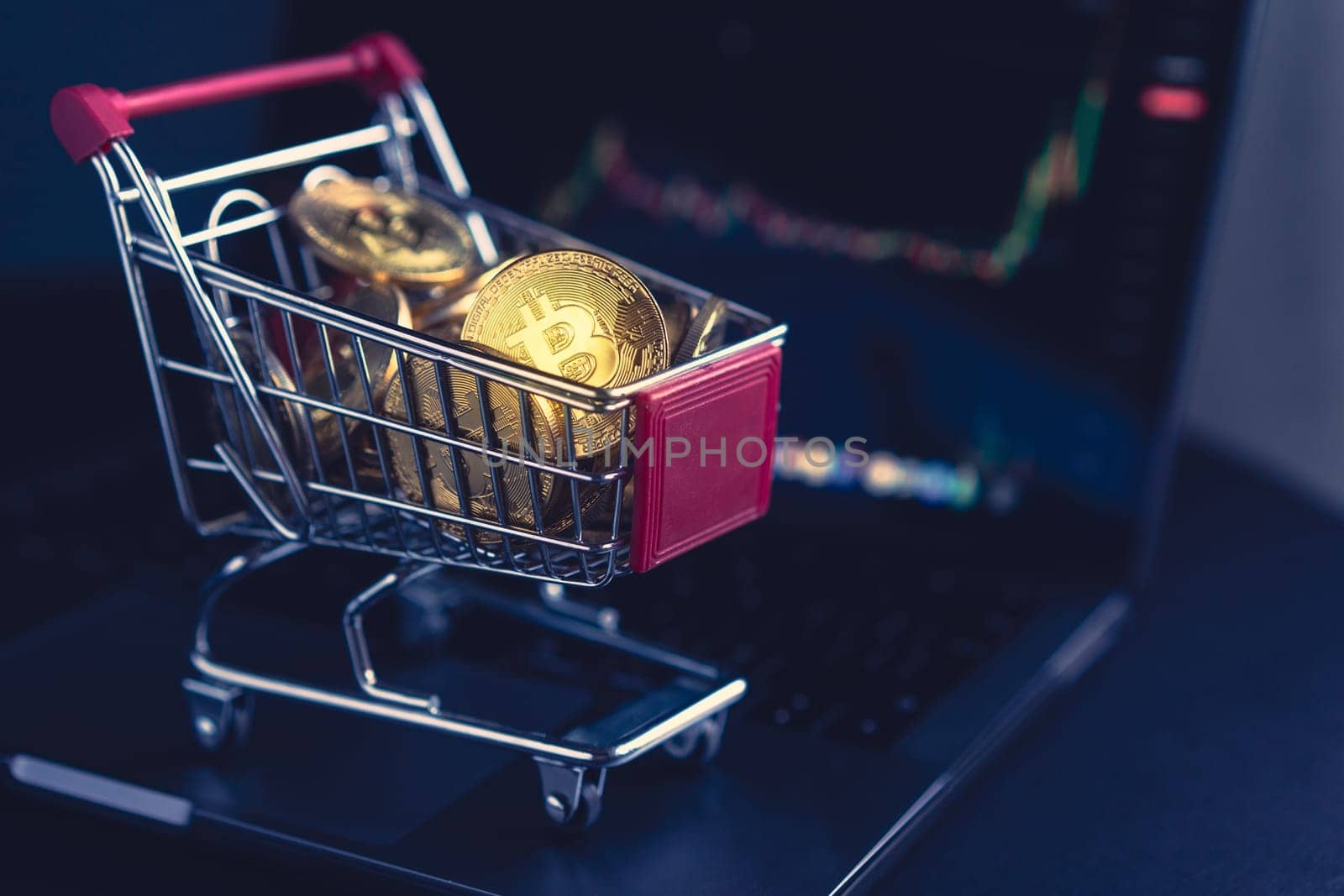 side view closeup cryptocurrency concept of market shopping cart full of bitcoin golden crypto coins standing near a notebook computer screen with trading graphics