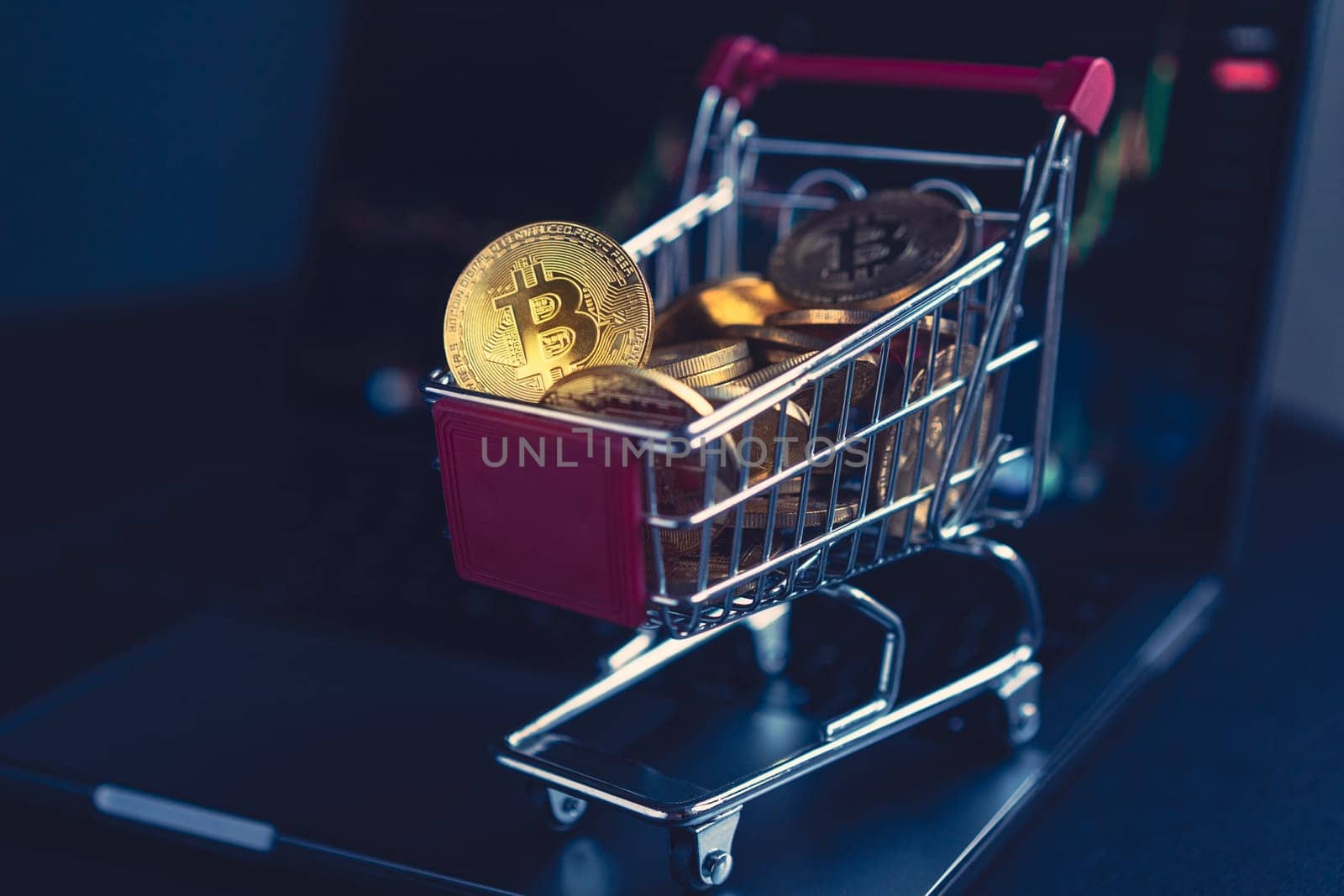 side view closeup cryptocurrency concept of market shopping cart full of bitcoin golden crypto coins standing near a notebook computer screen with trading graphics