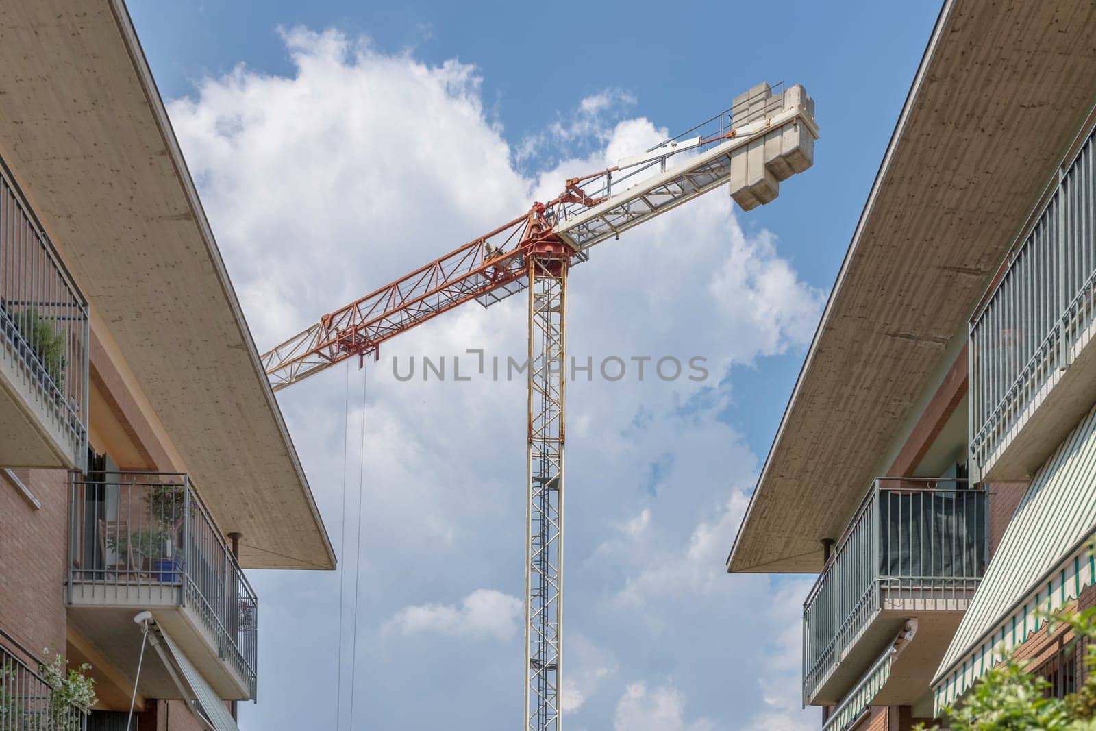 Huge industrial crane in the middle of apartments. Blue sky background with white clouds.