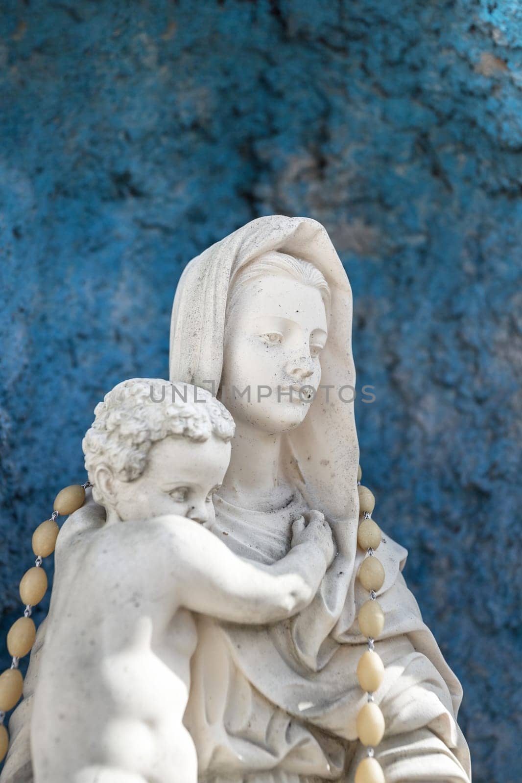 Statue of Our Lady of holy rosary and child Jesus. Blue rustic concrete on background.