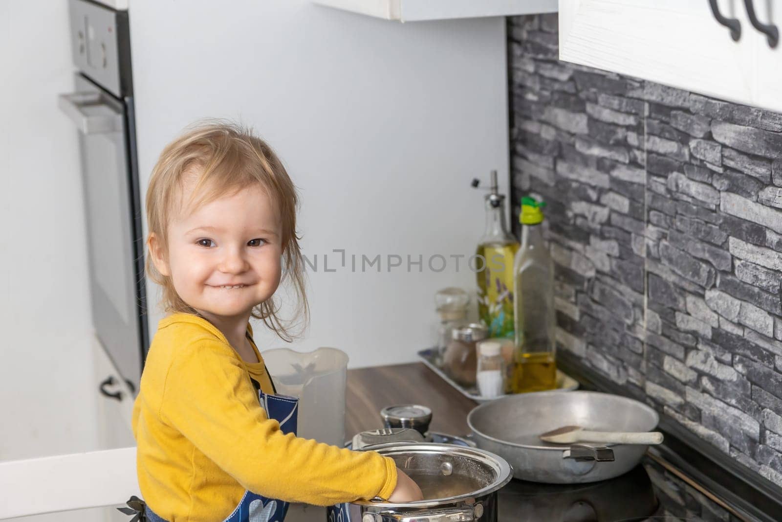 Cute little boy is cooking in the kitchen smiling at the camera. Horizontally.