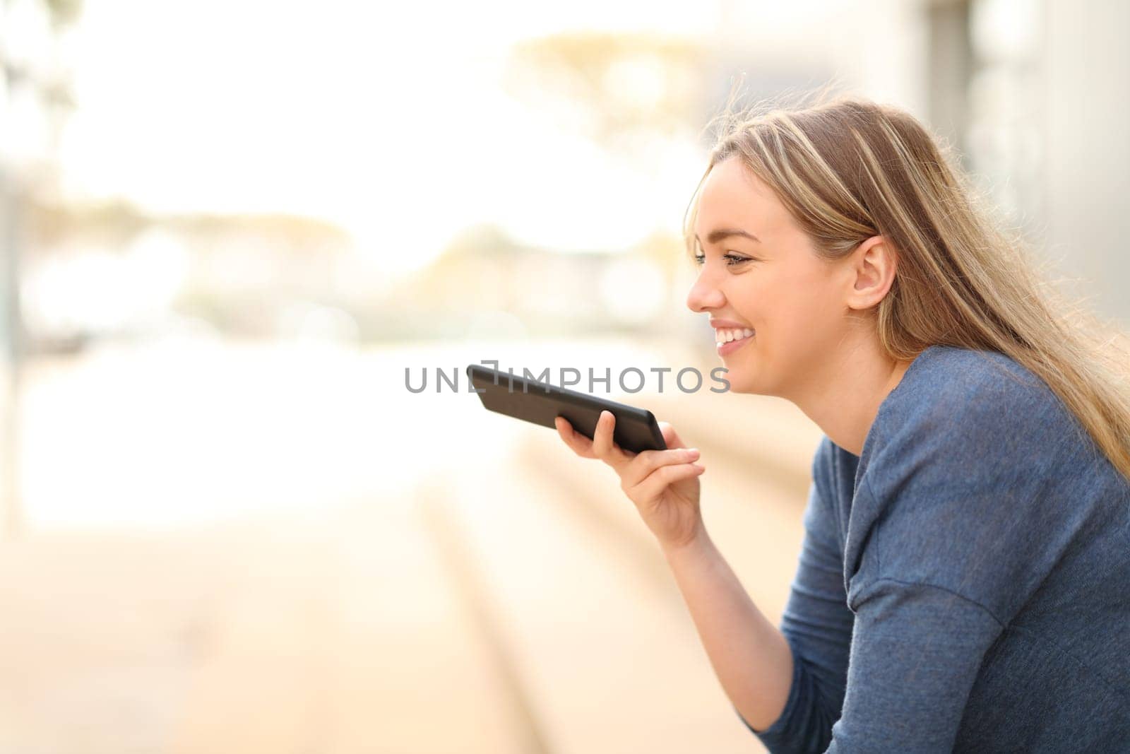Happy teen dictating a message on phone in the street
