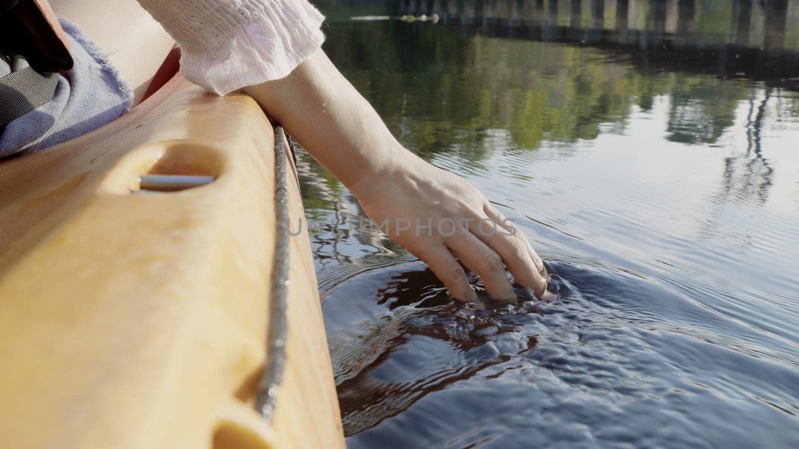 Close up back young adult woman hand on kayaking canoe boat on a lake touching a clear transparent water on summer day, adventure travel leisure enjoying concept, lifestyle sport vacation