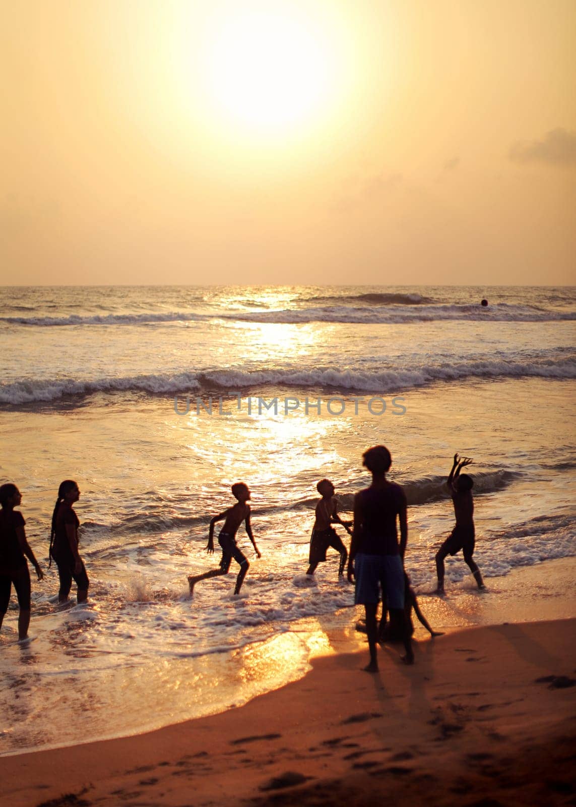 Kalutara, Sri Lanka - April 15, 2017: Silhouettes of people, mostly kids playing on the beach, sea and golden sunset afternoon light in background.
