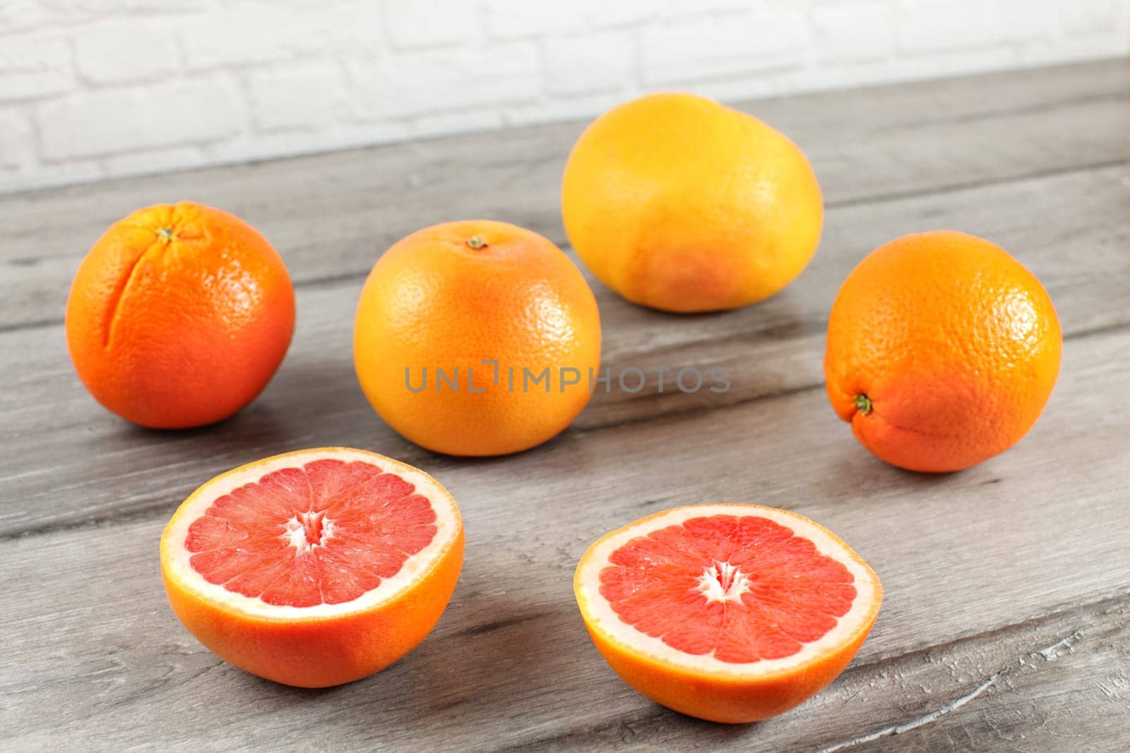 Pink grapefruit cut to half with more whole grapefruits and oranges in background on gray wood desk.