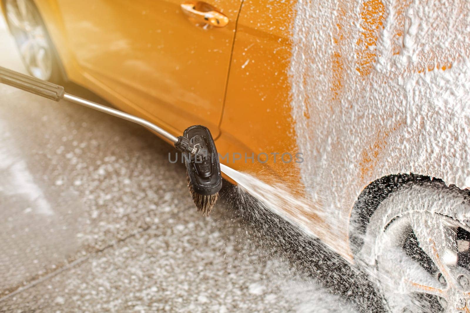 Foam and soap spraying from the brush onto rear wheel of car washed in carwash.