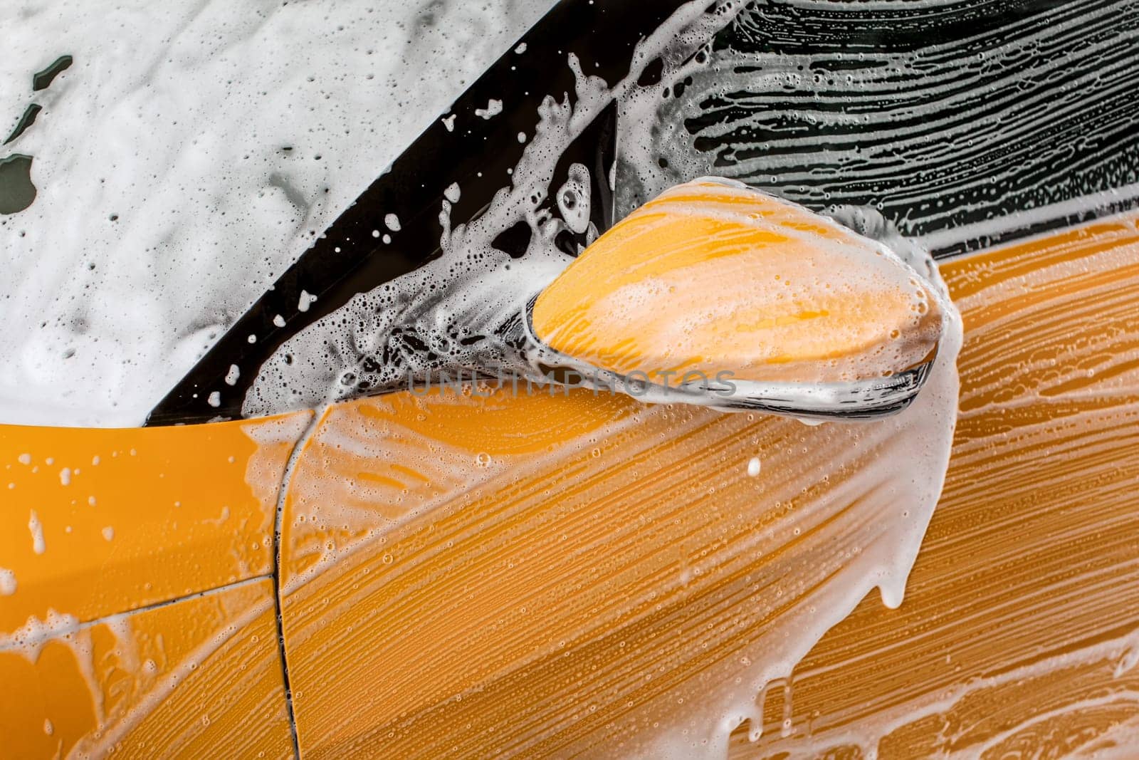 Detail on strokes left by brush in shampoo and foam, front mirror of a car washed in carwash.