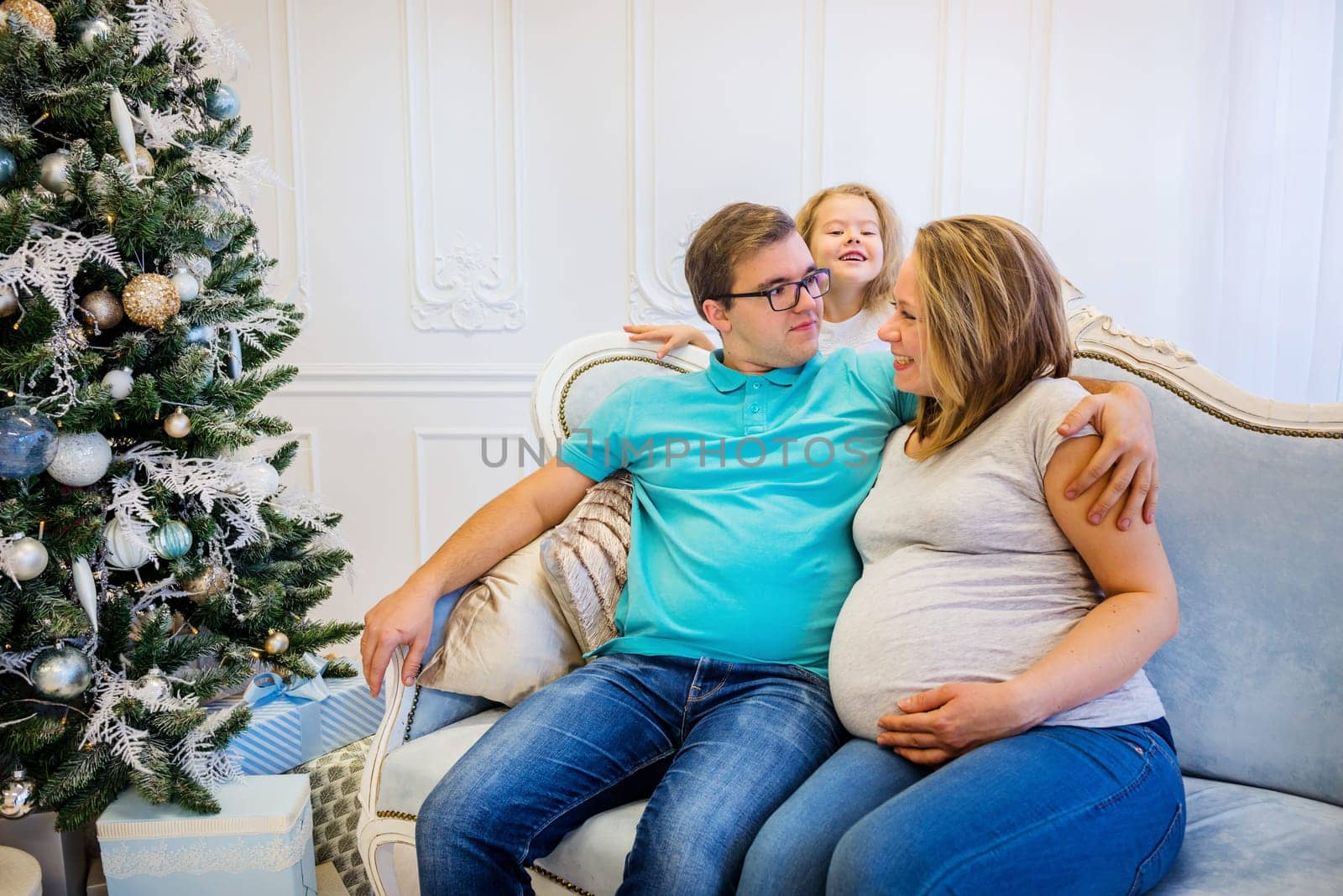 Family portrait near christmas tree. Pregnant woman. Funny daughter on the background.