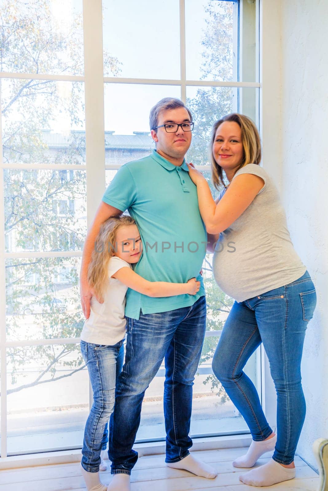 Beautiful pregnant woman, girl and man standing near the window