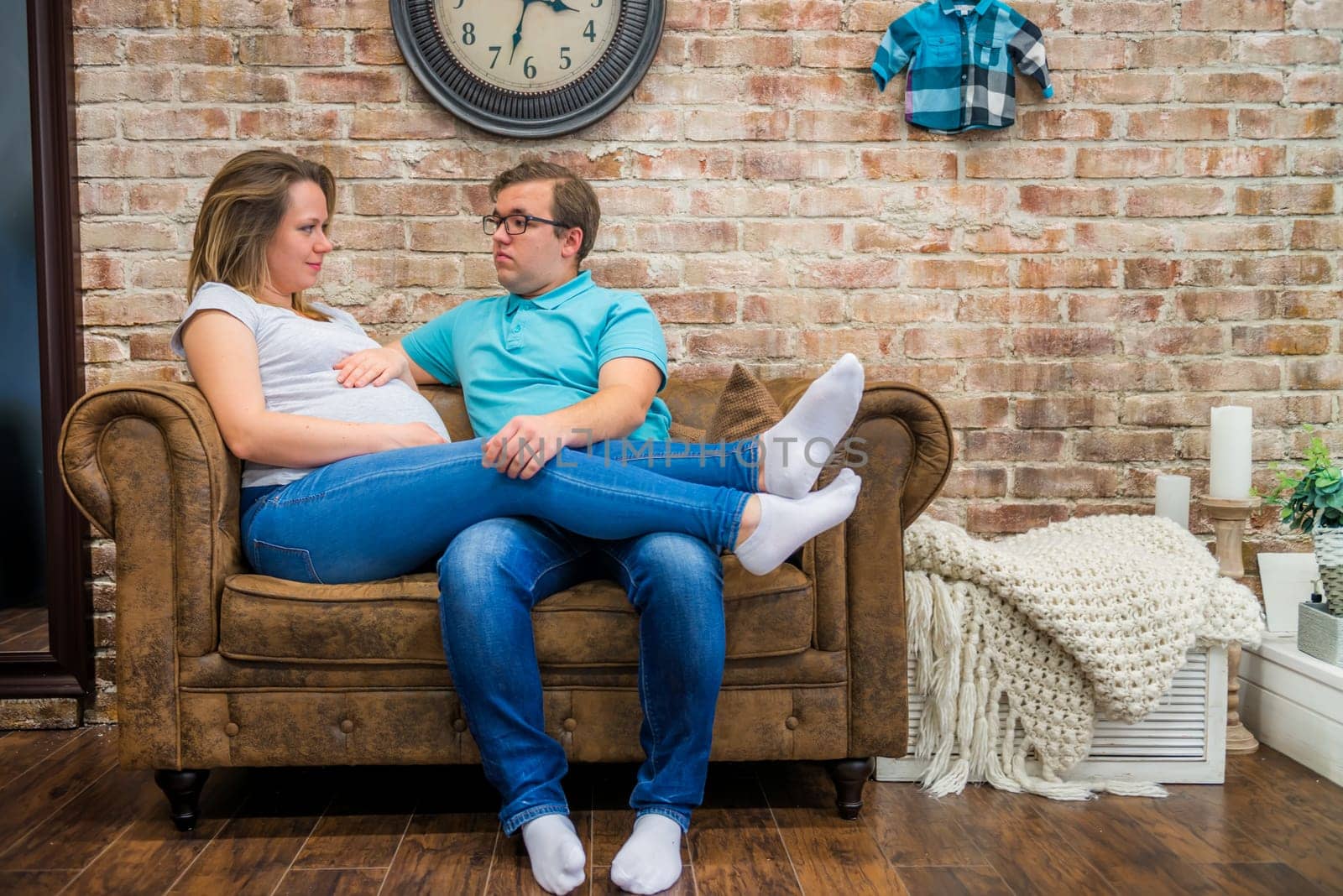 Beautiful pregnant woman and man sitting near brick wall