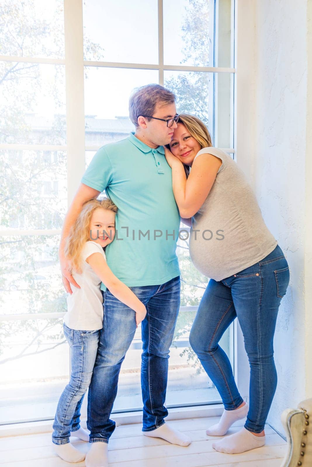 Beautiful pregnant woman, girl and man standing near the window
