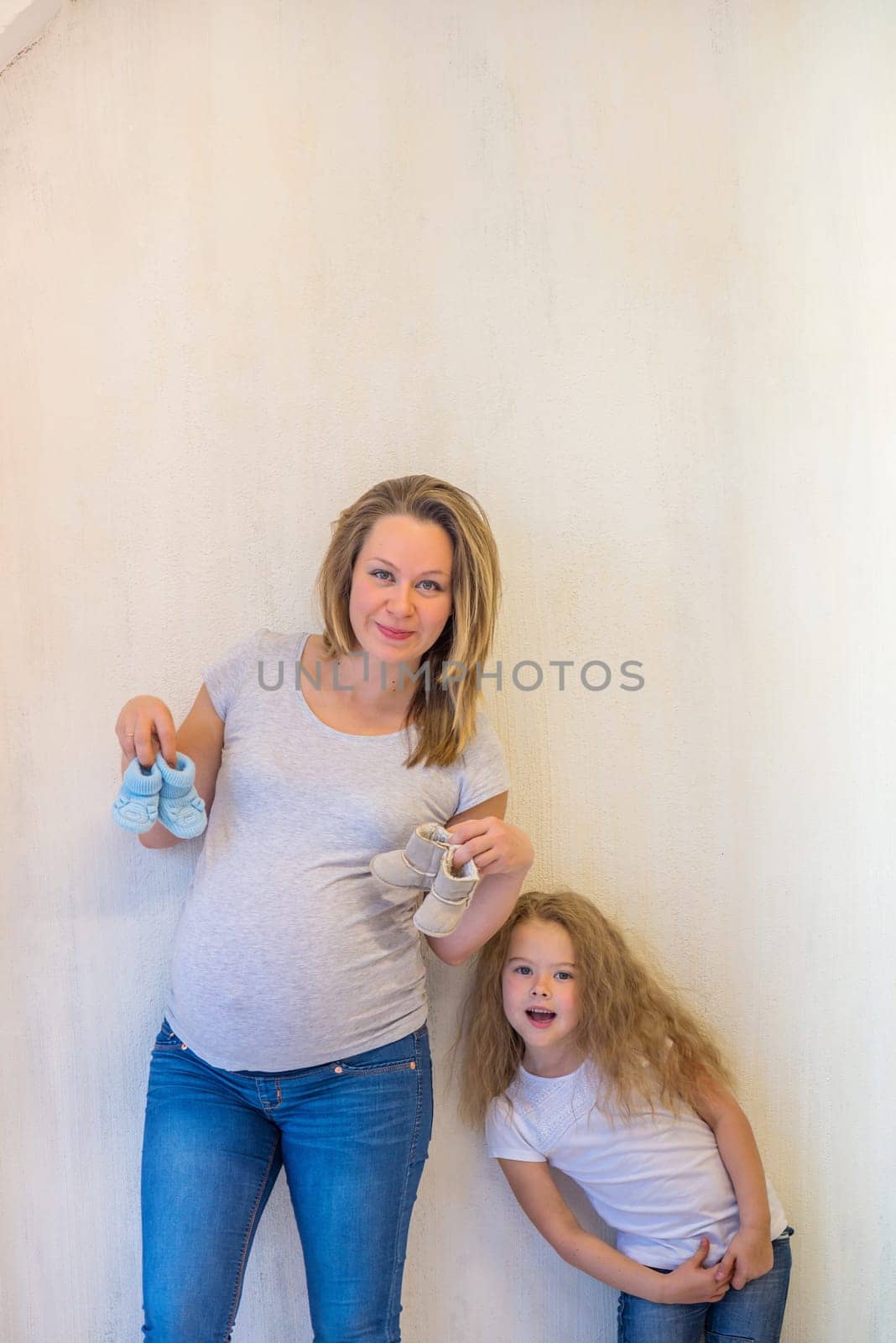 Pregnant woman holding blue baby booties with her daughter, expecting boy