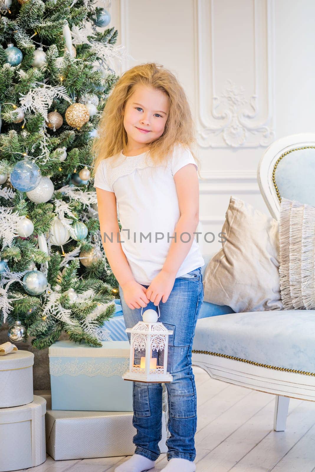 Cute girl in casual clothes and with old lantern on her hands near Christmas Tree