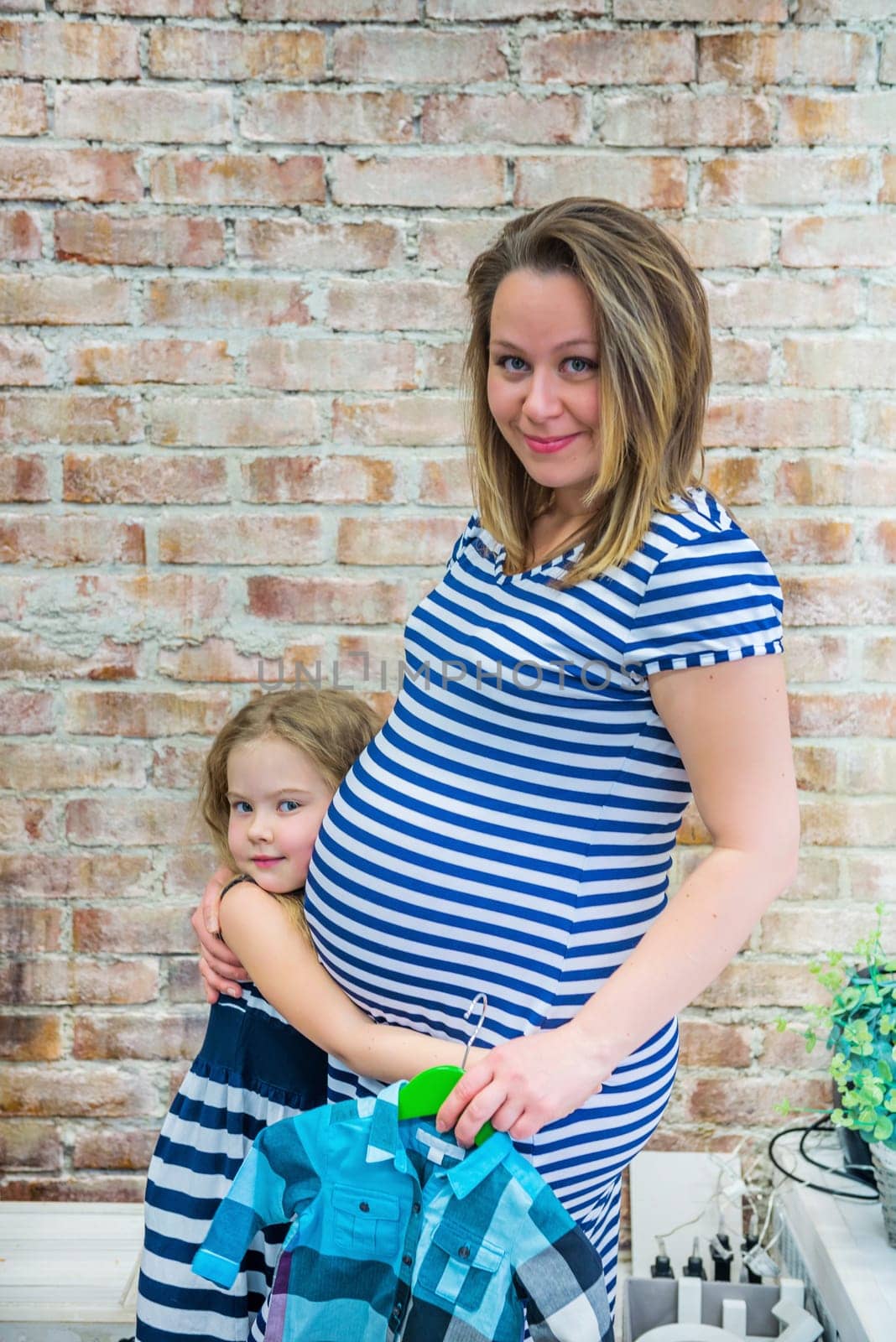 Beautiful pregnant woman with daughter near the brick wall