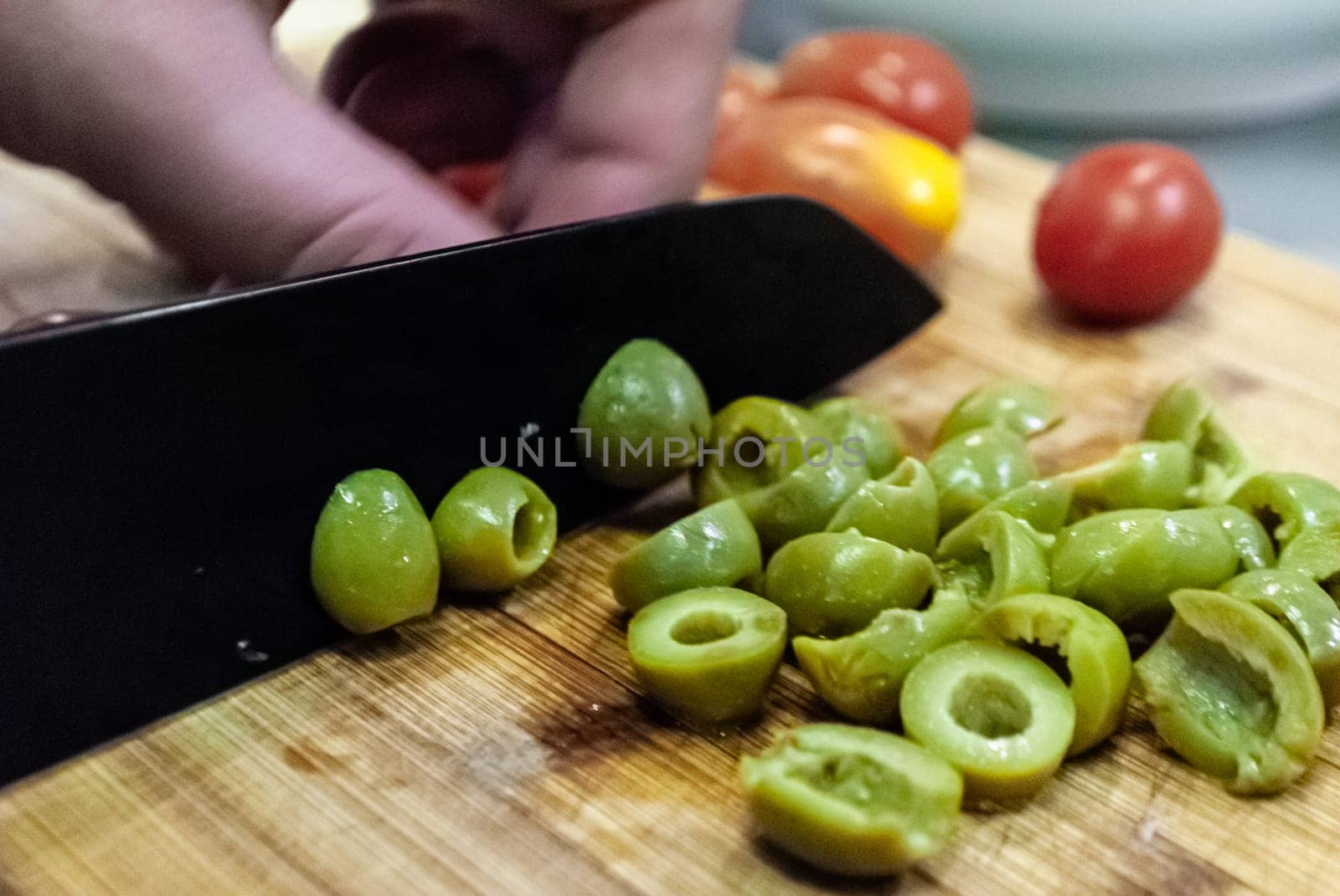 Step by step home cooking salad recepie. Kind of close, the man prepares a salad and cuts green olives on a wooden board