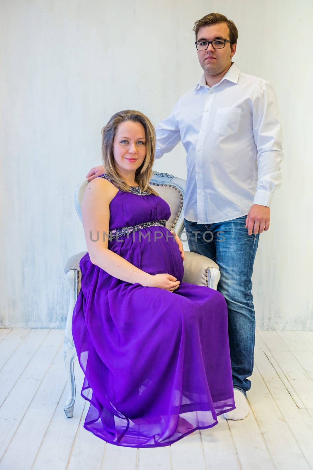 Pregnant woman in an ultraviolet dress with husband sitting on the chair