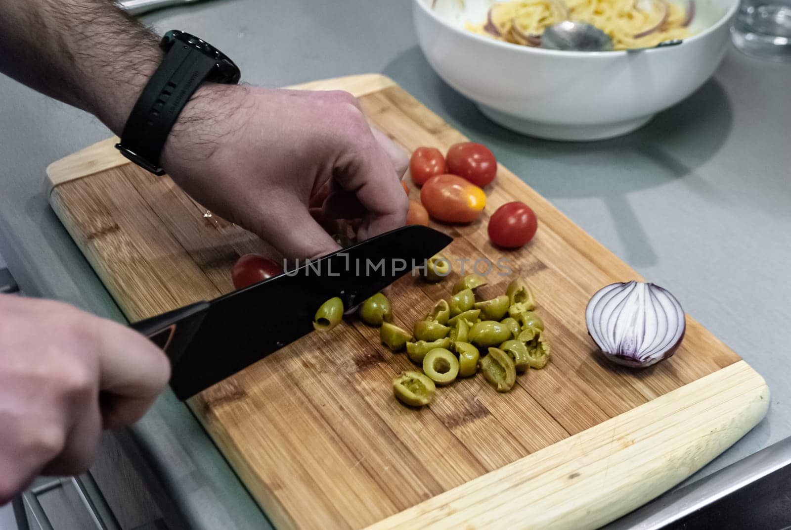 Step by step home cooking salad recepie. Man cuts green olives on wooden board in kitchen