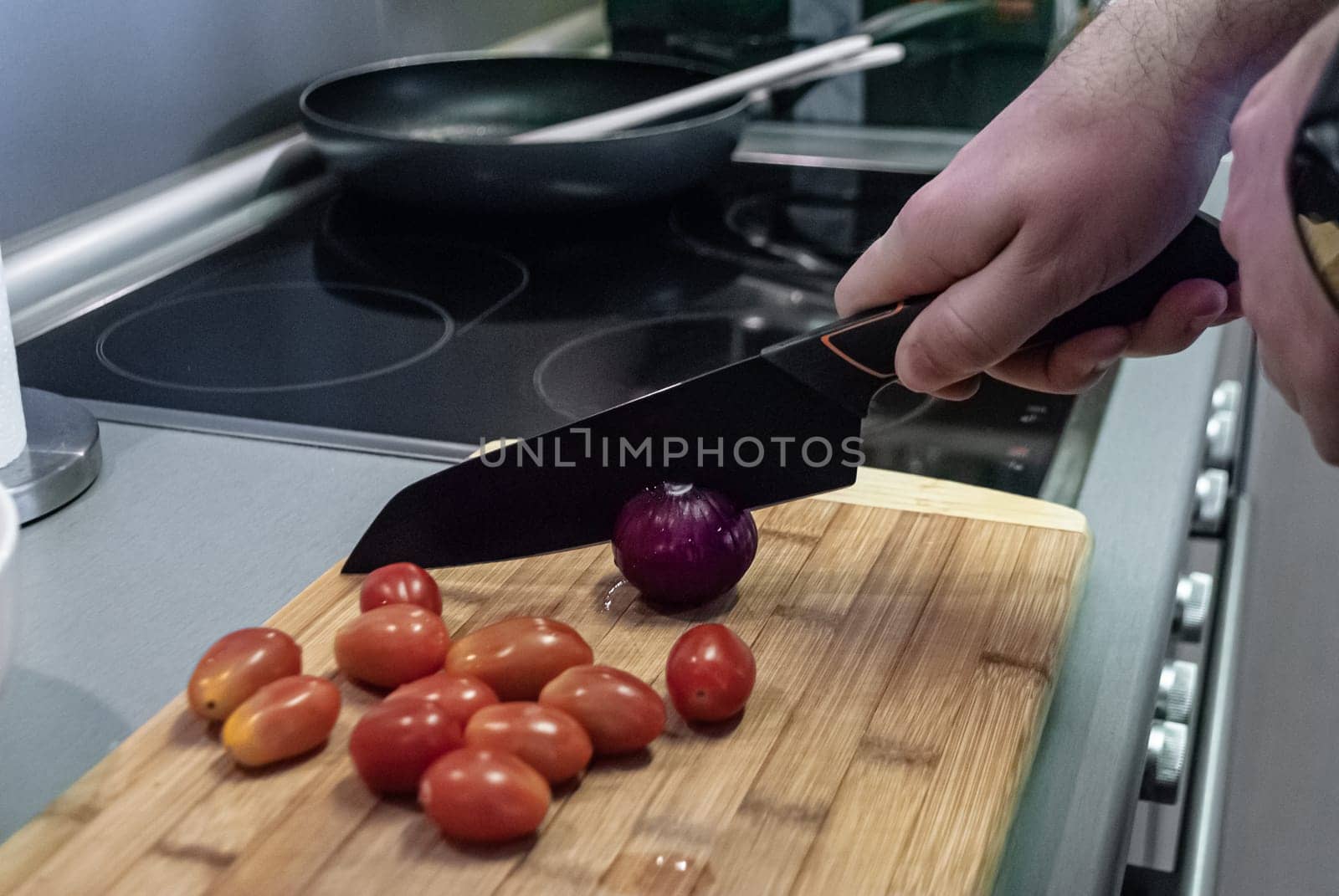 Step by step home cooking salad recepie. Man cuts red onion in kitchen of house against plate