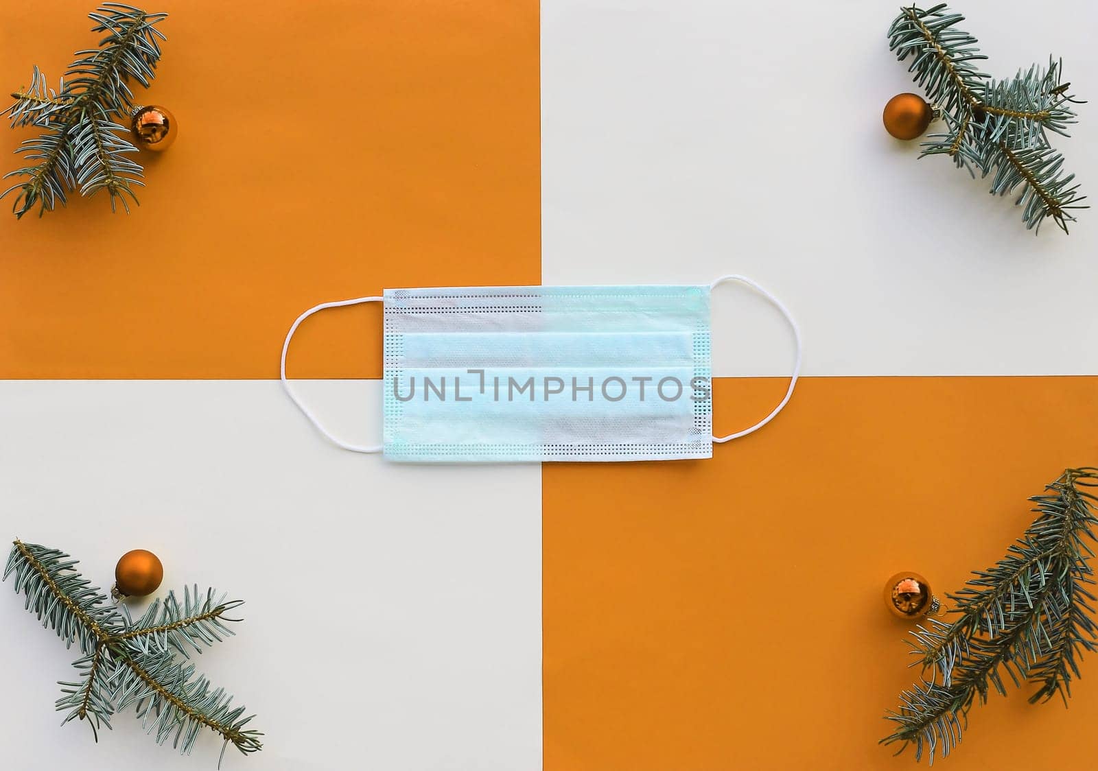 Corona and Christmas. A protective mask next to Christmas tree balls and fir branches on an orange and beige background