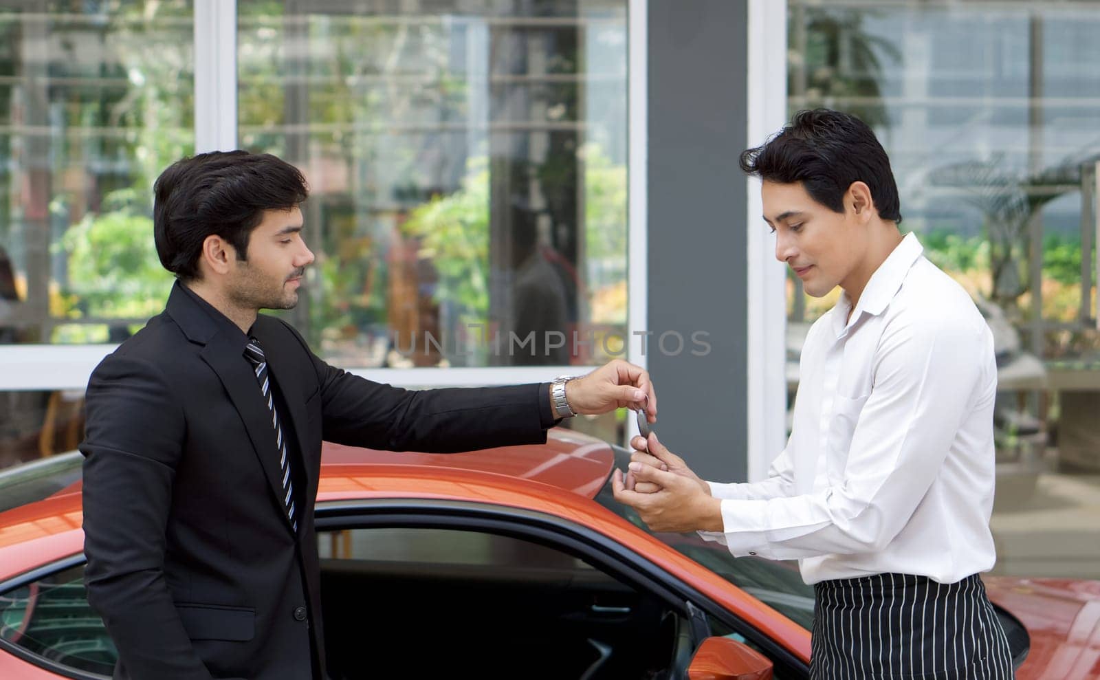 Young businessman in a black suit handling sport car key to the valet service staff.