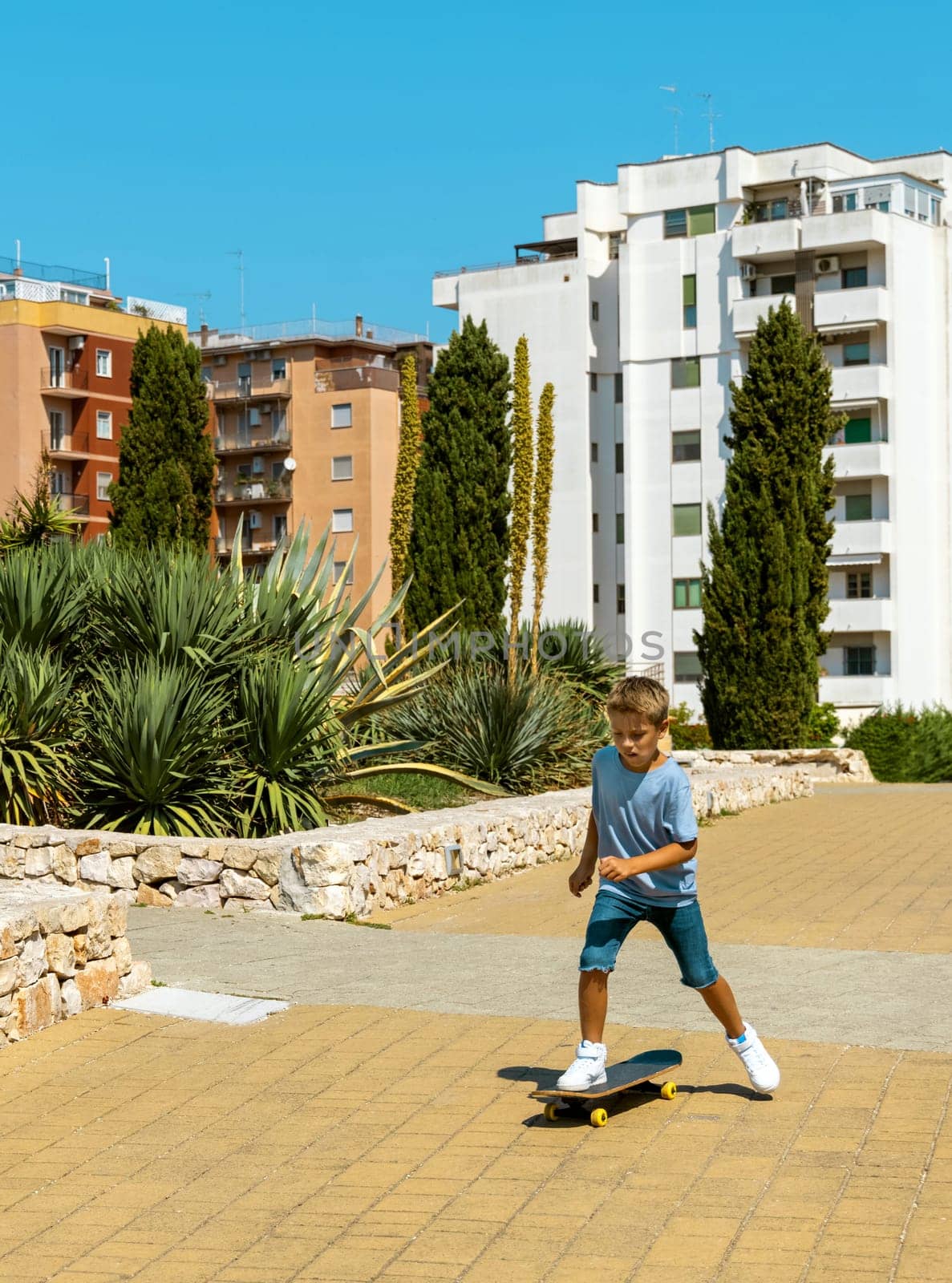 Preschooler kid boy in blue t-shirt learning to ride a skateboard outdoors. Cute child doing sports and having fun in park. Active hobbies, healthy lifestyle concept. T-shirt mockup