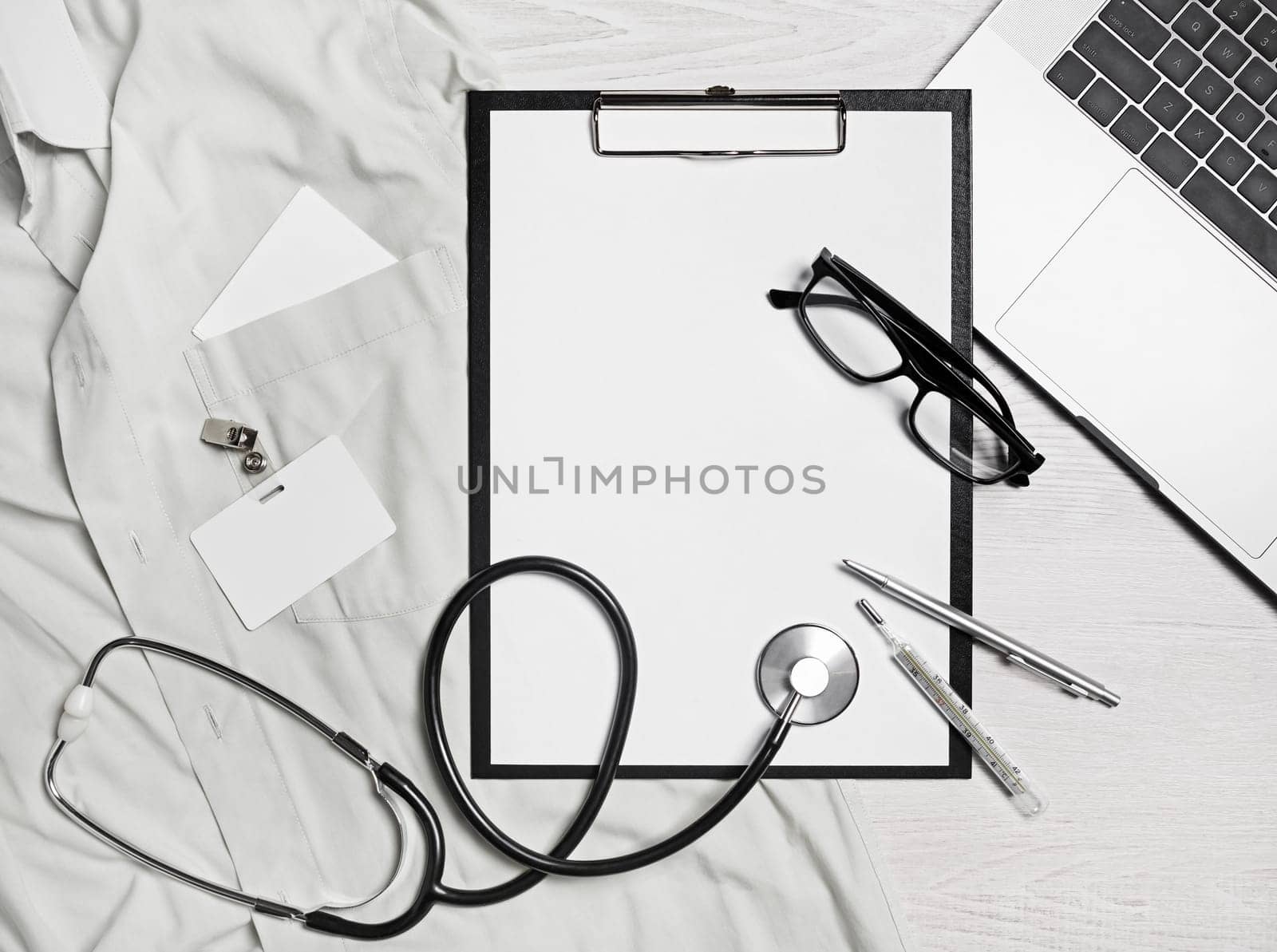 Health care concept. Blank medical clipboard, stethoscope, glasses, badge, thermometer, pen and laptop. Flat lay.