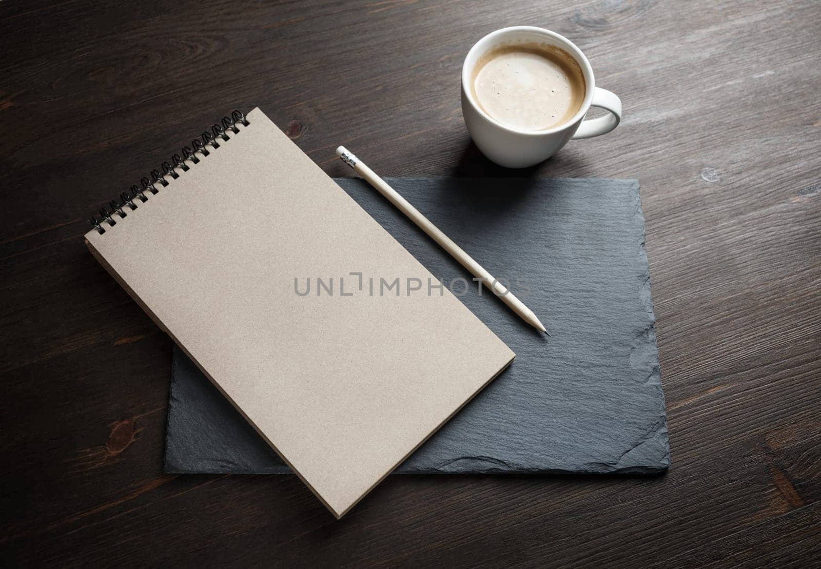 Blank kraft sketchbook, pencil and coffee cup on stone board. Responsive design mockup.