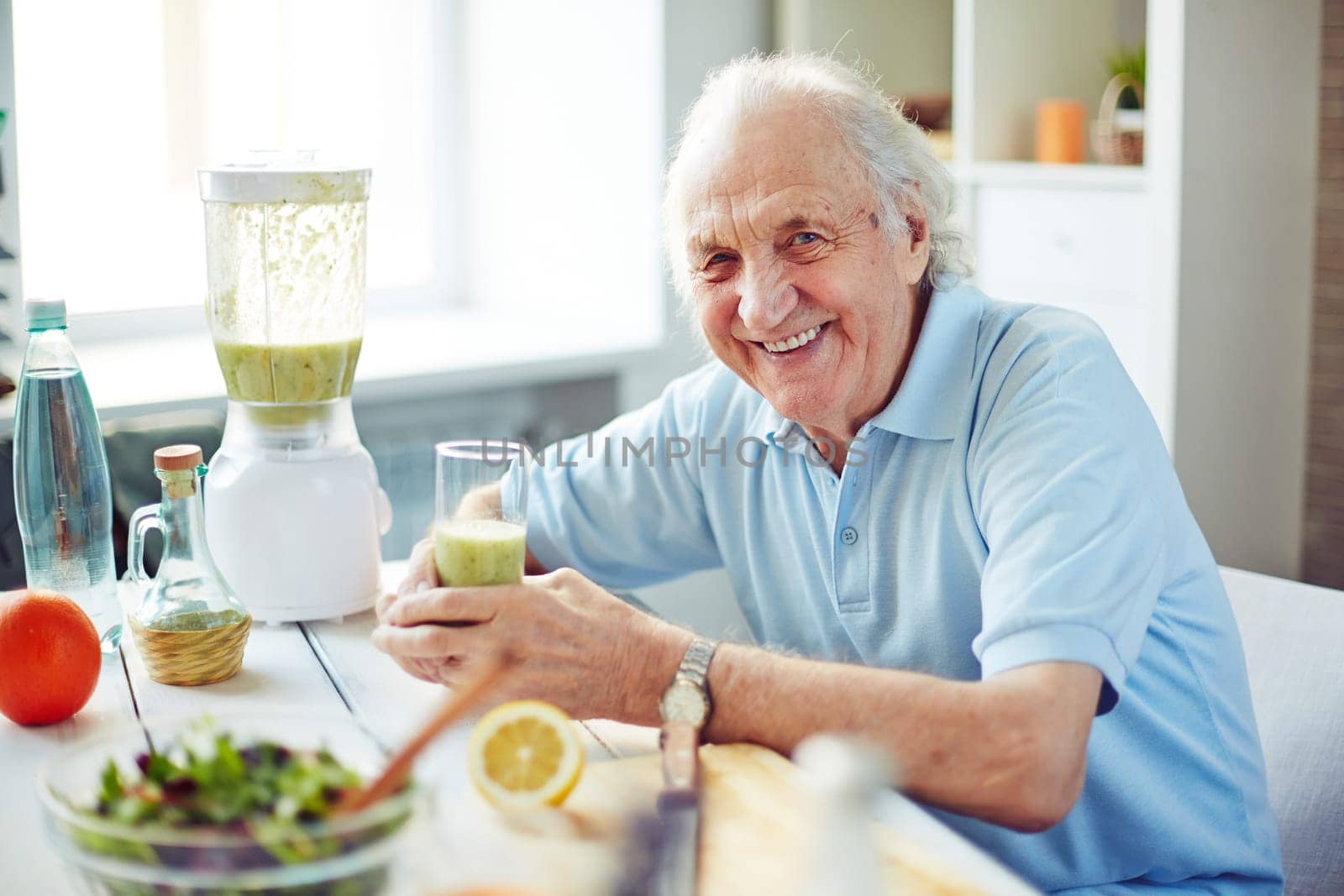 Senior man with glass of fruit smoothie sitting in kitchen