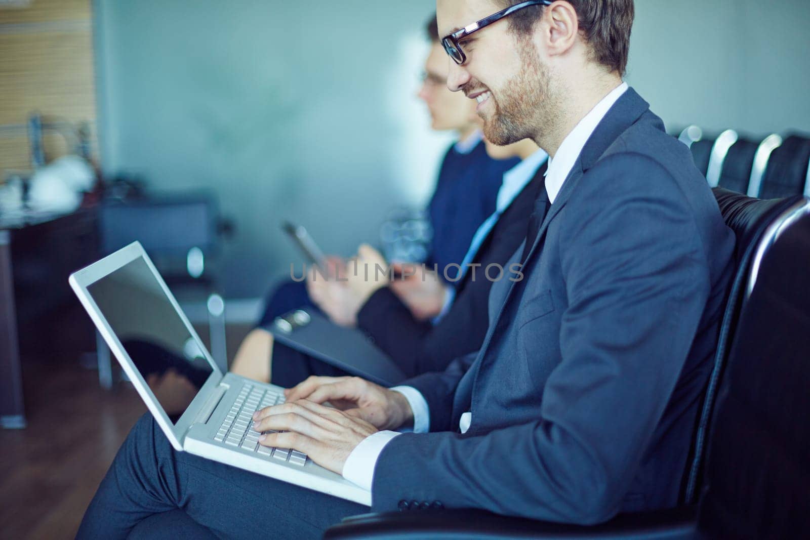 Young businessman typing at seminar on background of other employees