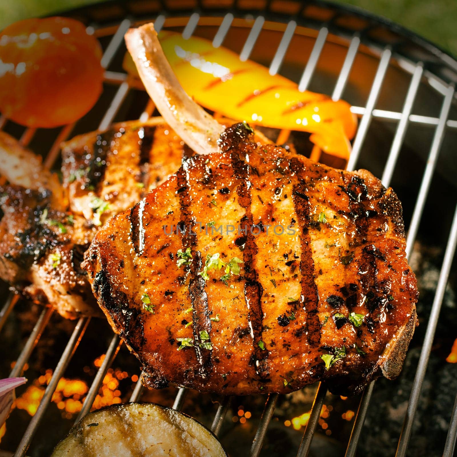 Delicious crispy barbecued marinated and seasoned pork loin cutlets with eggplant and tomato cooking on a grill , close up view of the meat