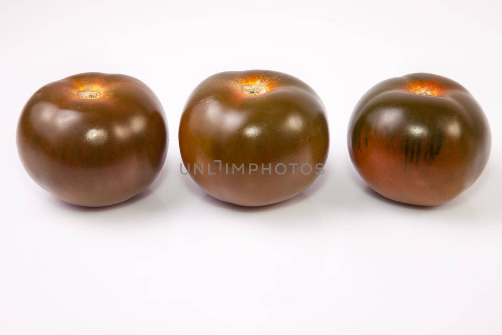 Three dark green kumato tomatoes. Isolated over white background