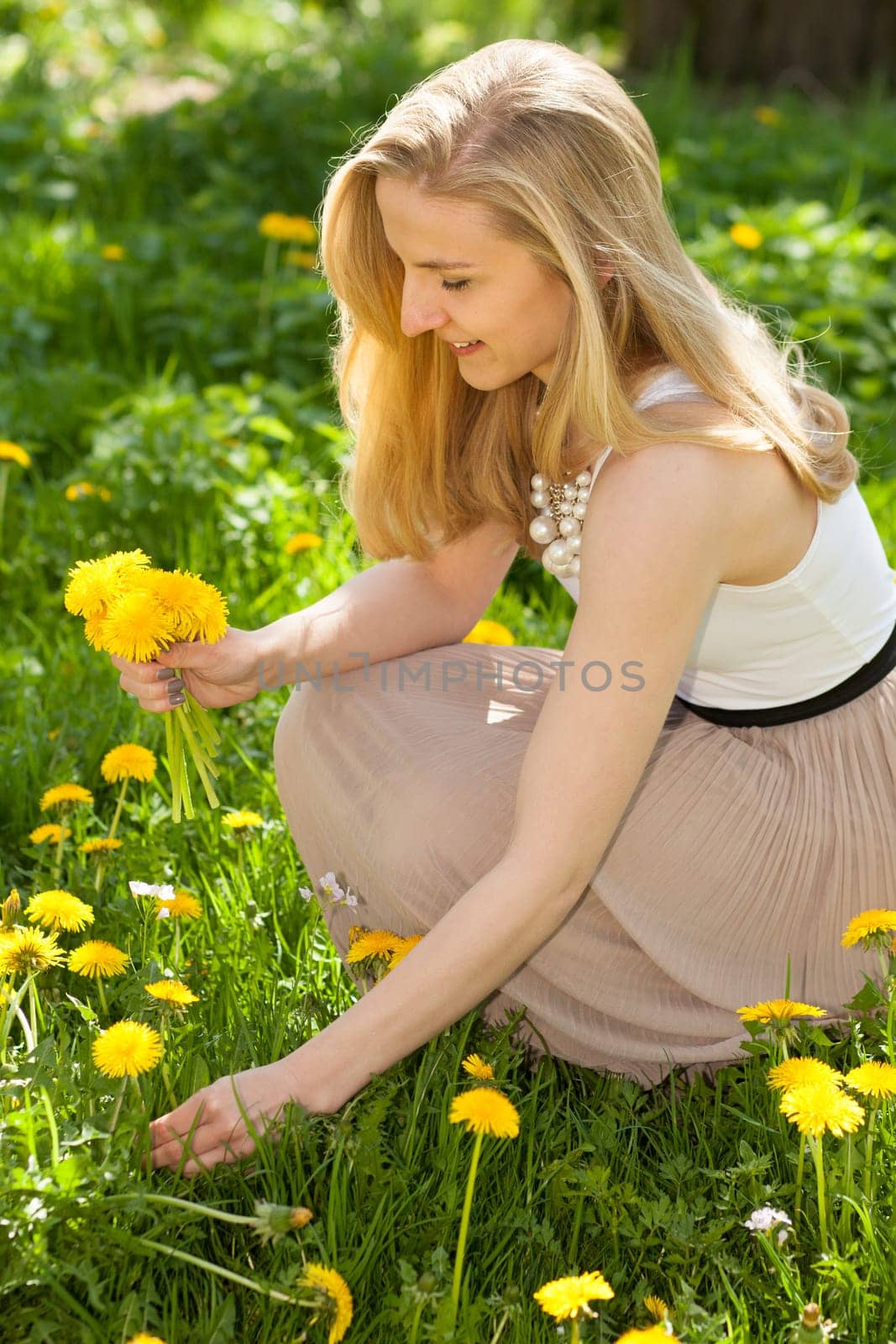 Young woman picking dandelion in spring in a meadow