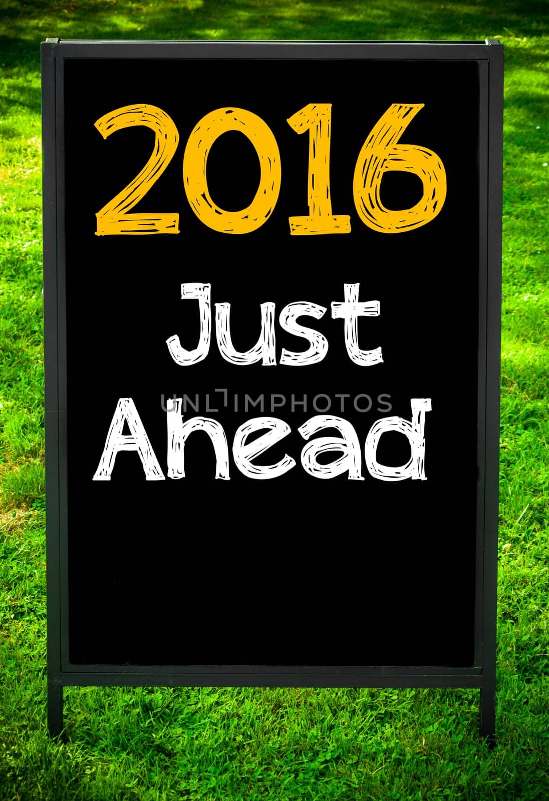 2016 JUST AHEAD  message on sidewalk blackboard sign against green grass background. Copy Space available. Concept image