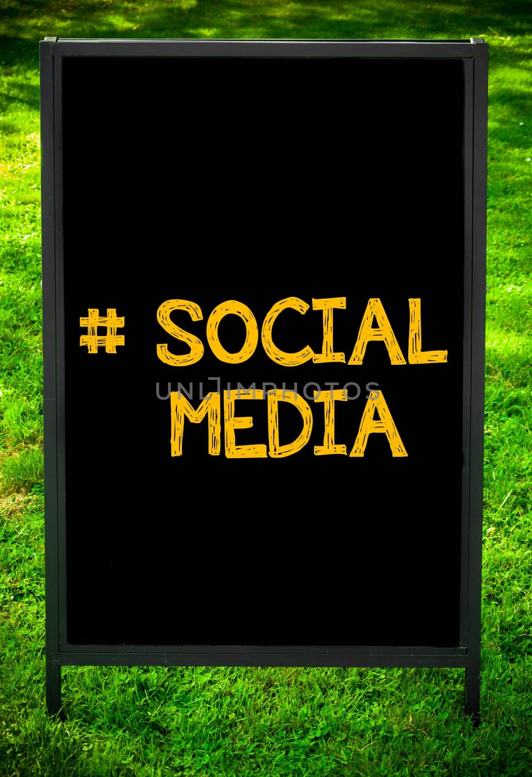 Hashtag Social Media message on sidewalk blackboard sign against green grass background. Copy Space available. Concept image