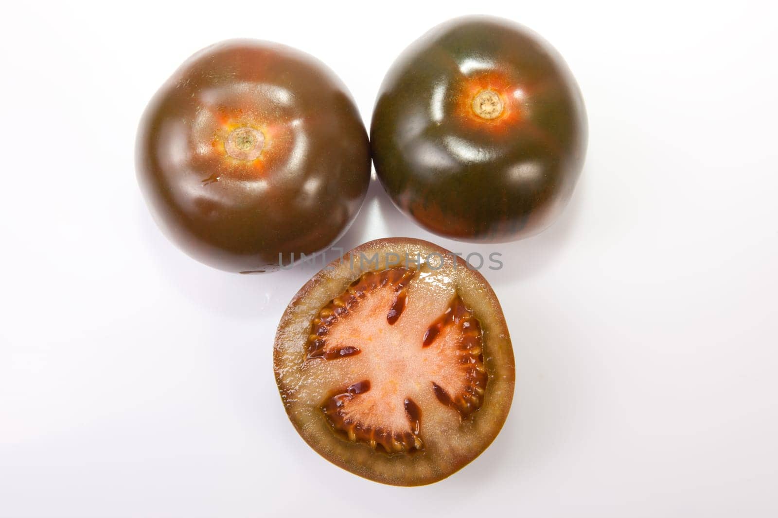 Dark green kumato tomatoes, whole and sliced. Isolated over white background