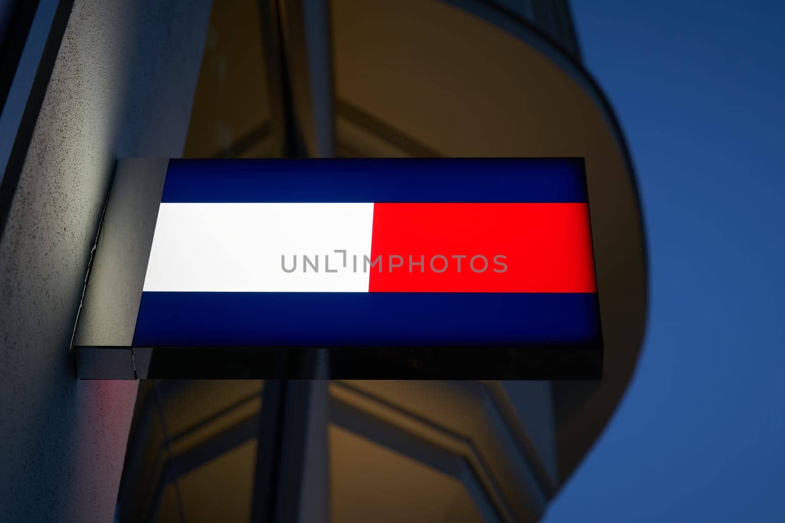 Neon light with the logo of fashion designer Tommy Hilfiger in a shopping street in Berlin in the evening