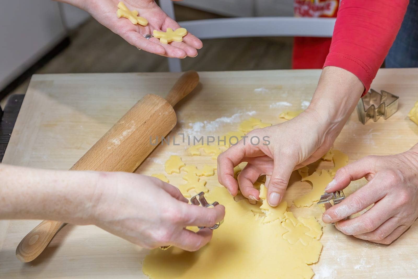 Two women cut out cookies from dough in domestic kitchen, indoors. Horizontally.