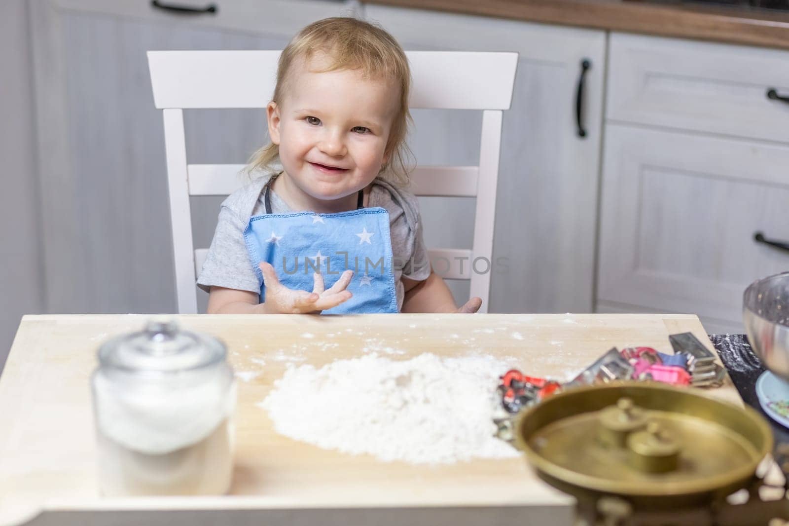 Llittle cute boy is posing at the table ready to bake cookies in the kitchen.
