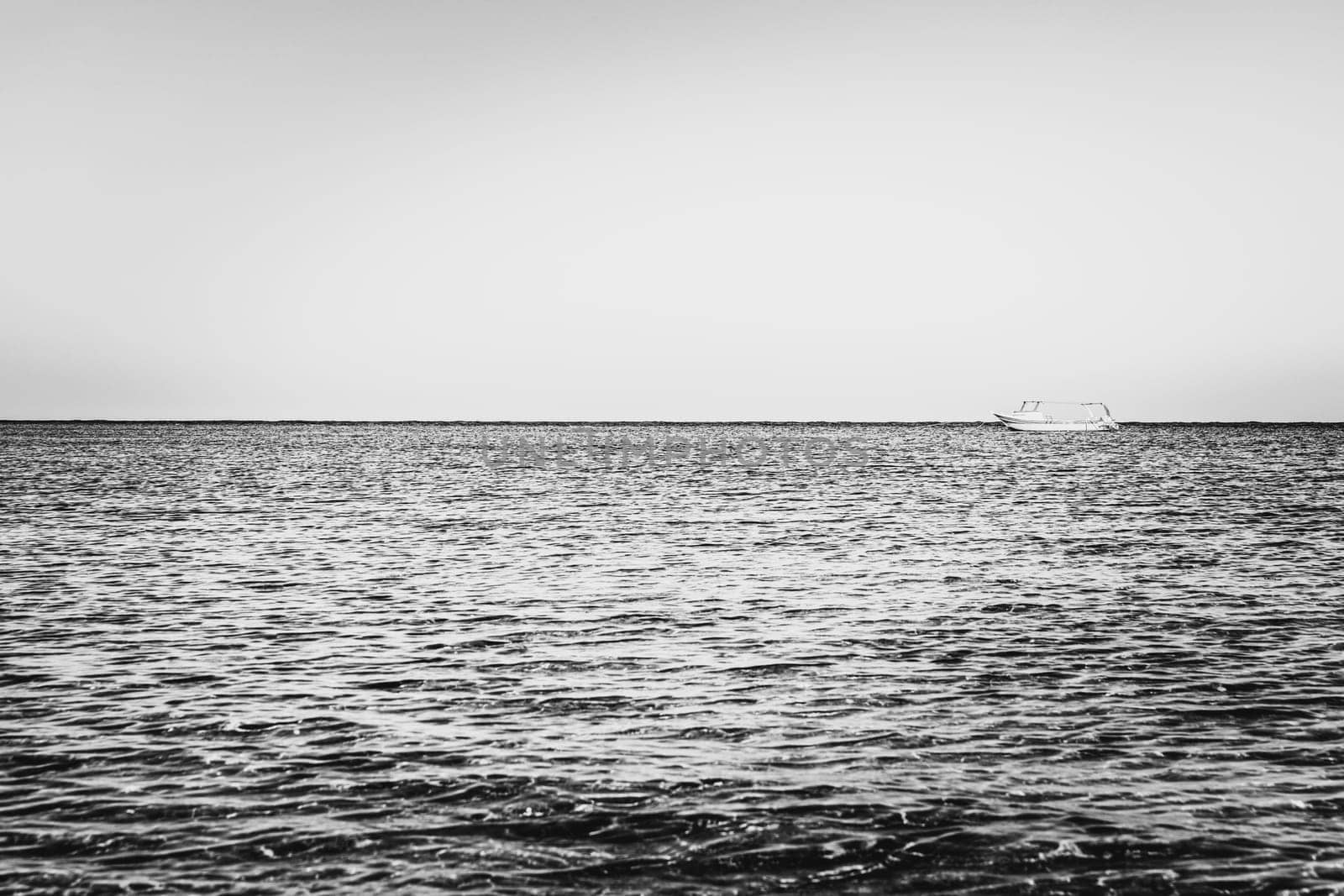 Black-white vessel or yacht photography. Alone white boat or ship in silent sea or ocean water surface. A quiet and peaceful harbor or bay. Small waves making tranquil mood. Transportation business