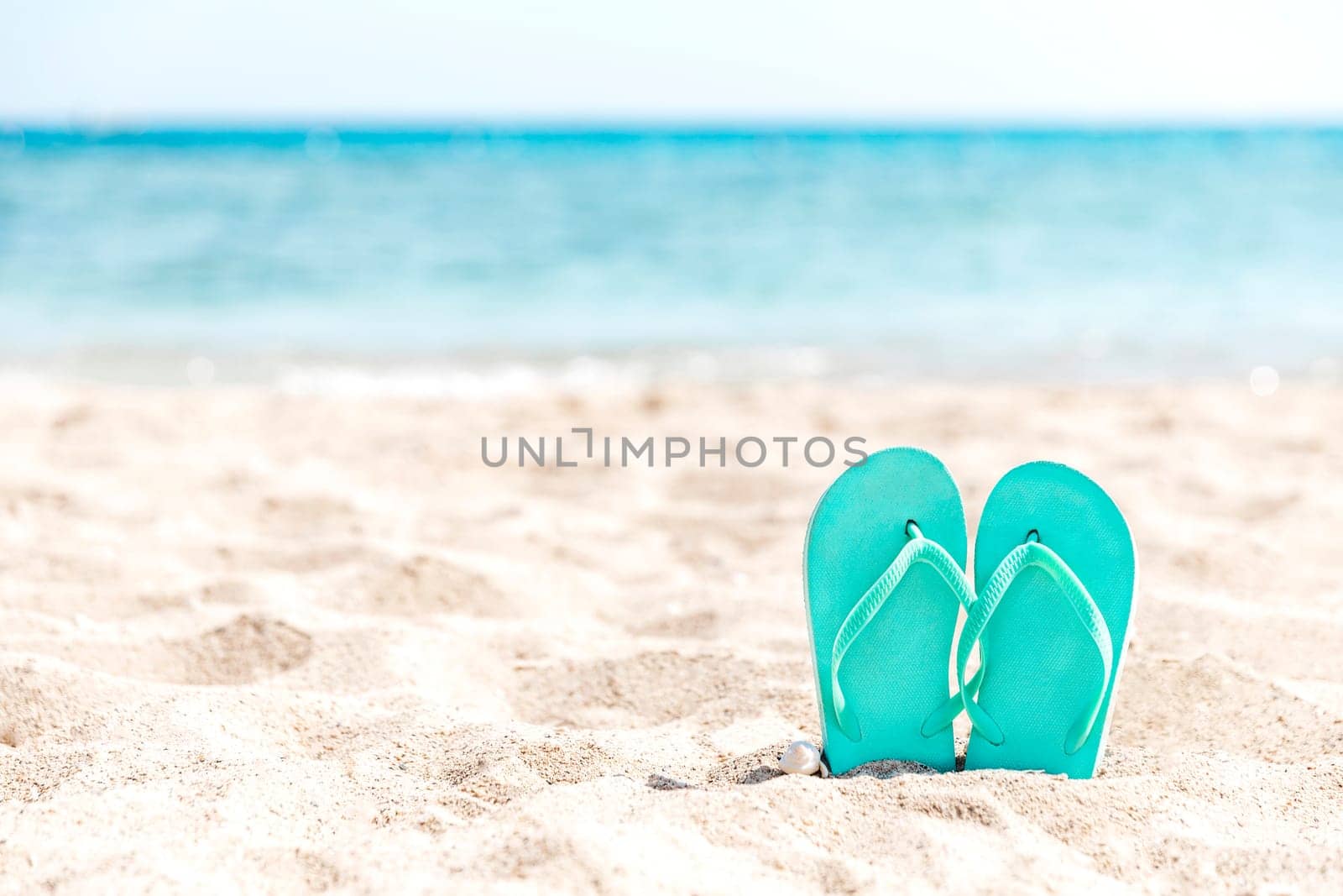 Turquoise or light blue flip flops or sandal shoe stuck in the sand on sandy beach by the sea coastline or ocean. Travel or vacation concept in hot countries in summer or winter. High quality photo