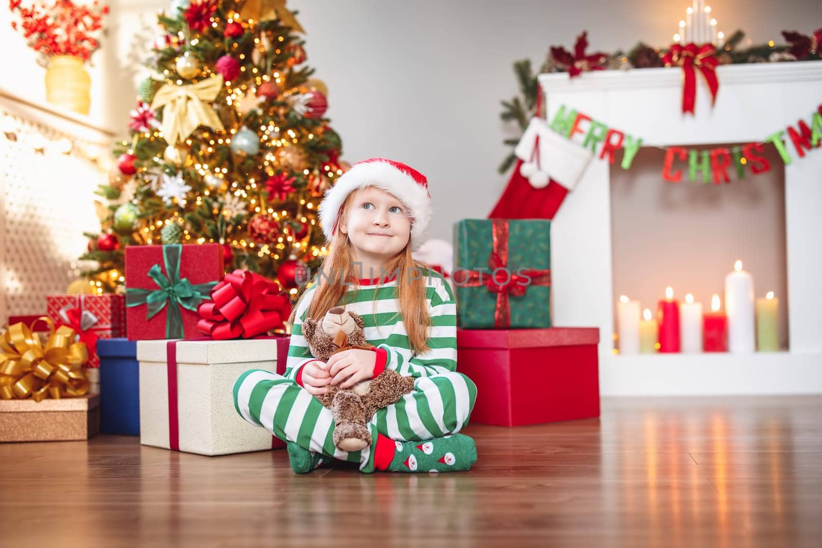 Cute little girl sitting in the room with christmas decoration. Child near christmas tree
