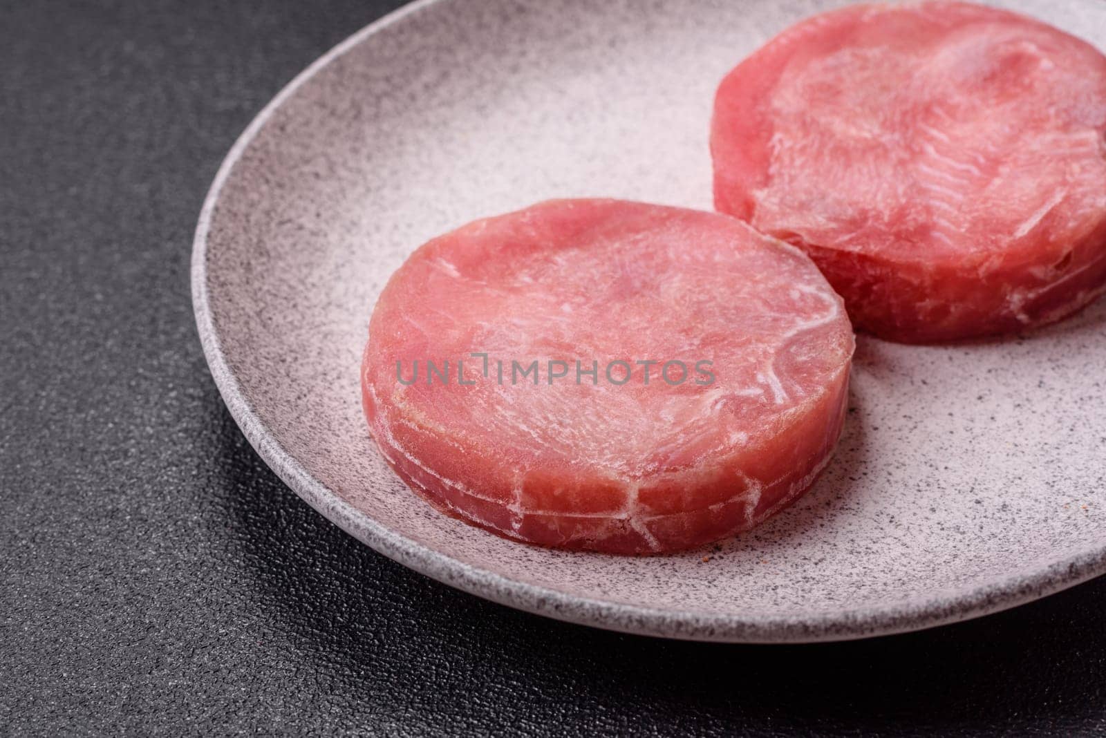 Two fresh slices of raw tuna fillet with spices and herbs on a dark concrete background