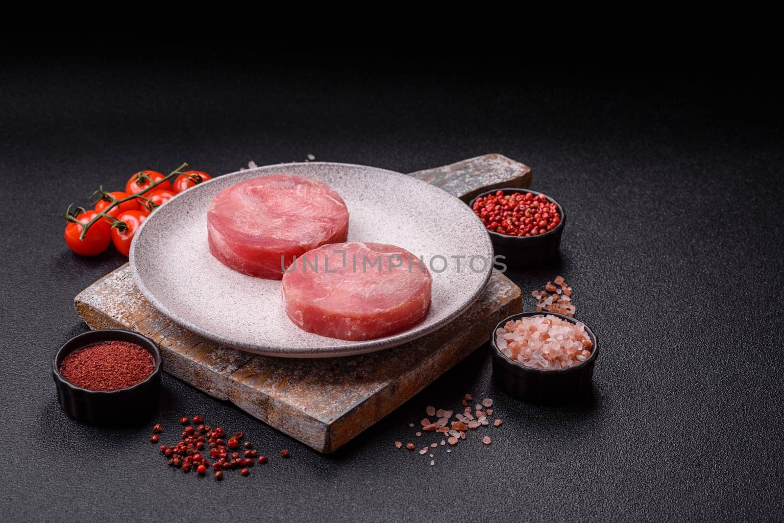 Two fresh slices of raw tuna fillet with spices and herbs on a dark concrete background