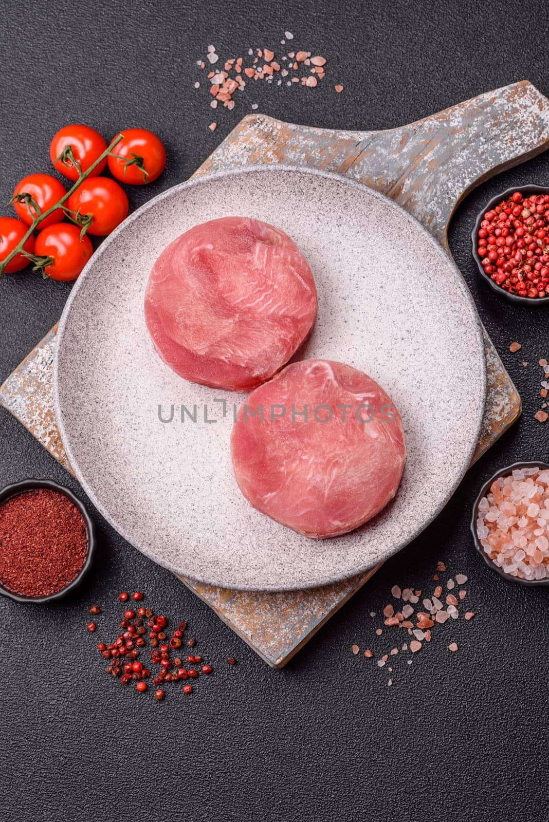 Two fresh slices of raw tuna fillet with spices and herbs on a dark concrete background