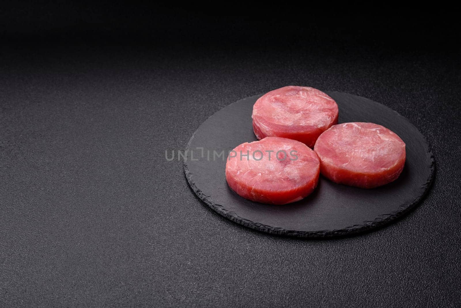 Two fresh slices of raw tuna fillet with spices and herbs on a dark concrete background